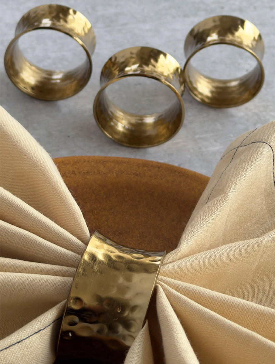 Set of hammered gold napkin rings with one holding a cream napkin
