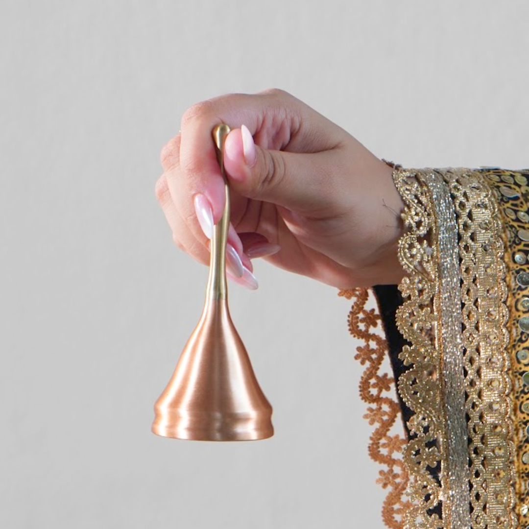 Hand holding a brass and copper prayer bell by its slender handle