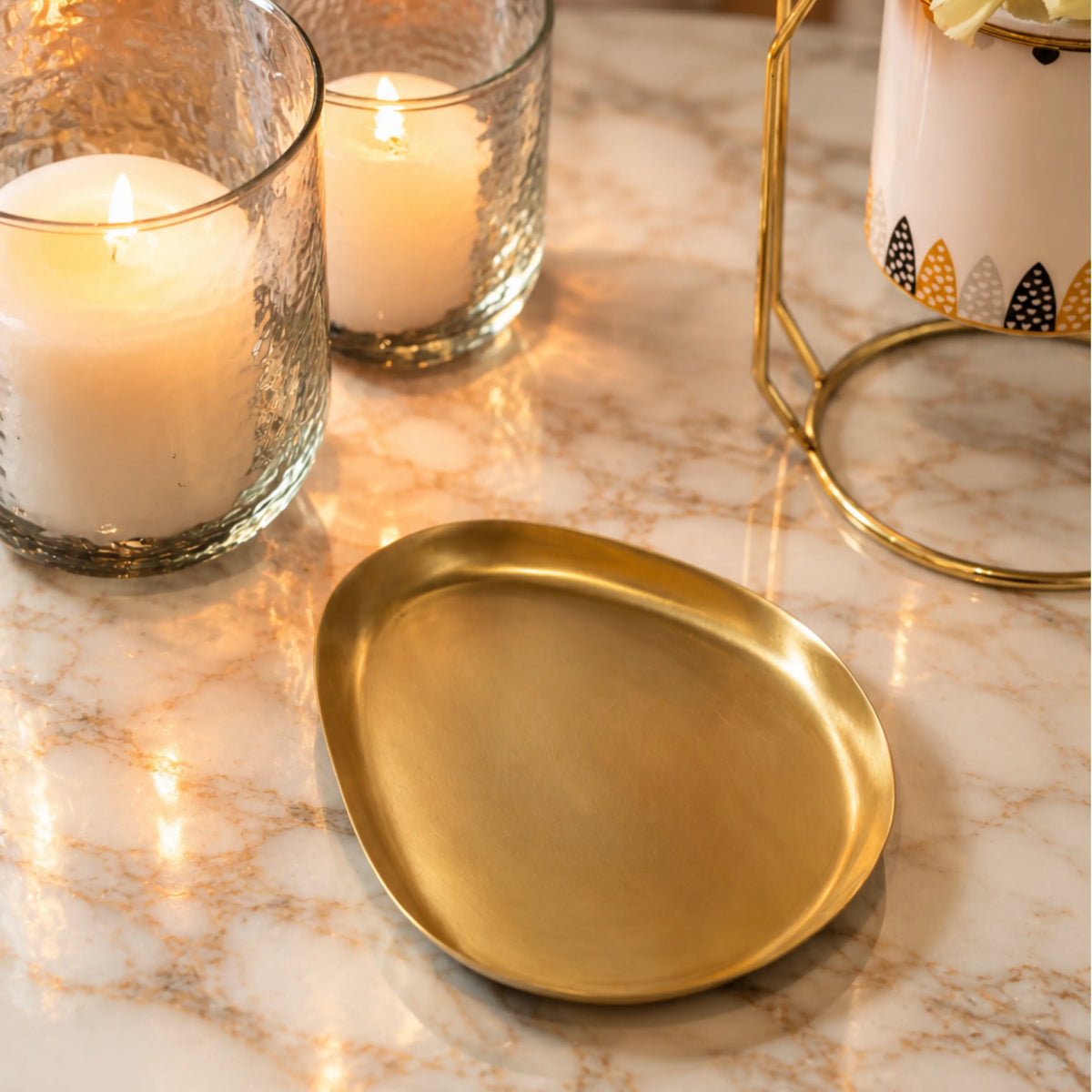 Brass snack plate beside glass candle holders on a marble table