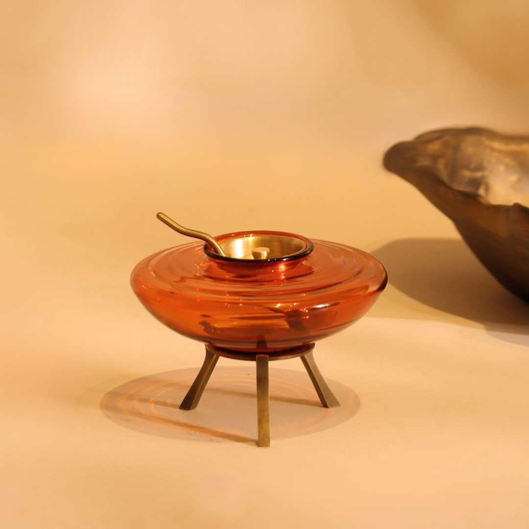 Amber glass ghee dani with brass spoon on a dining table