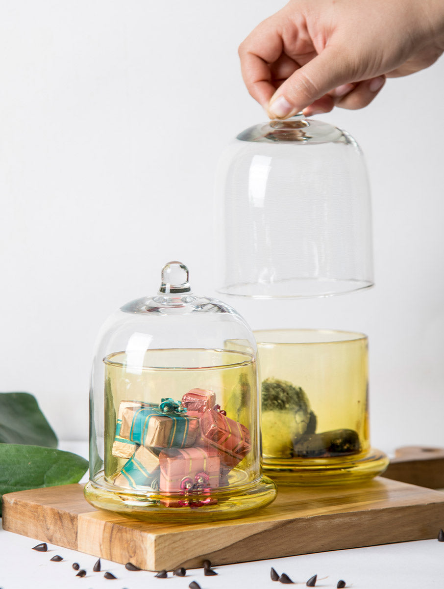 Yellow glass bell jars filled with wrapped chocolates and treats, one lid lifted