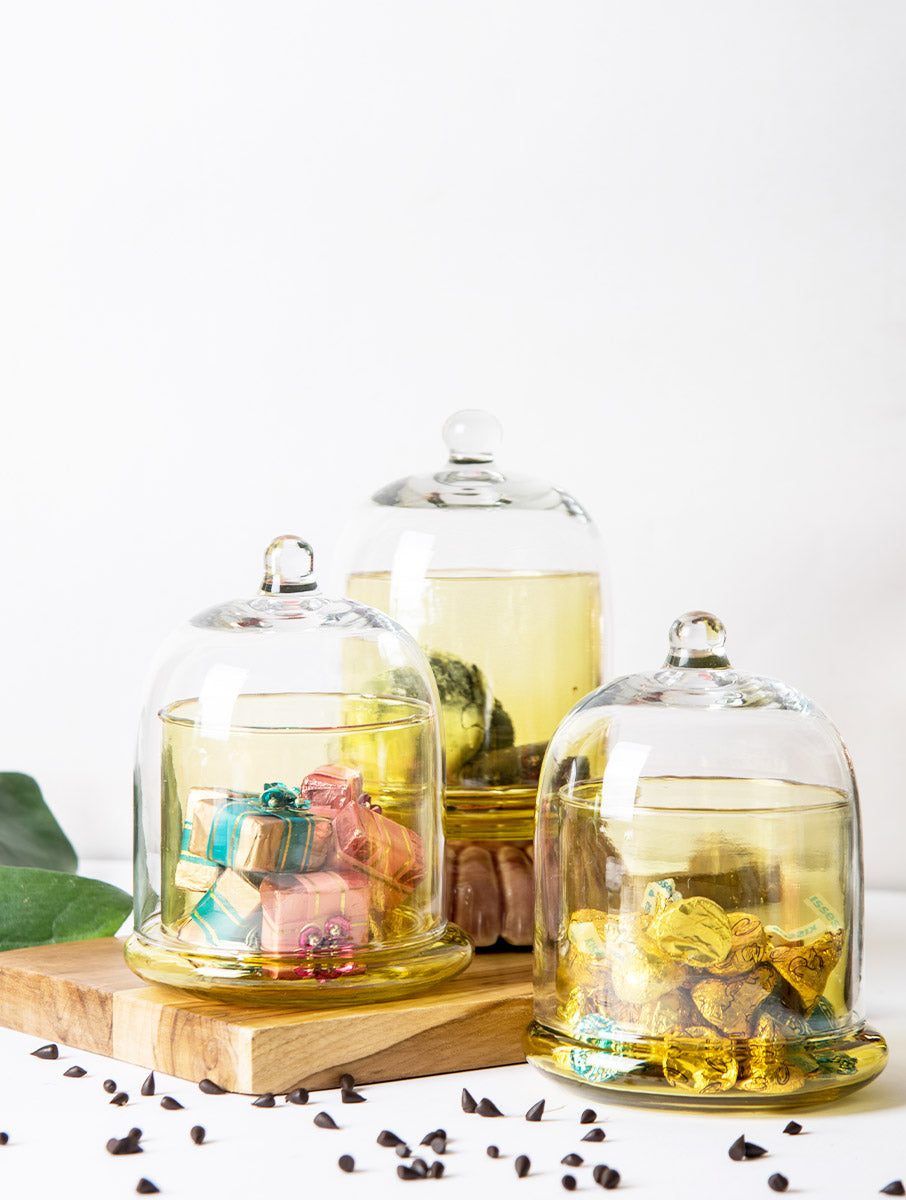 Three honey-yellow glass bell jars holding chocolates, sweets and treats