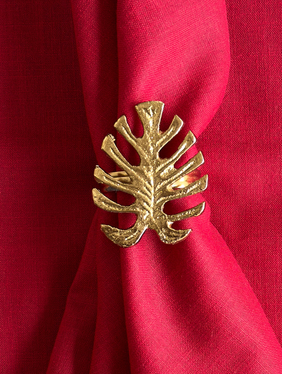 Close-up of a gold monstera leaf napkin ring on a red linen napkin