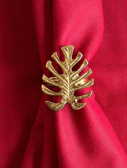 Close-up of a gold monstera leaf napkin ring on a red linen napkin