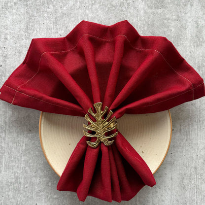 Gold monstera leaf napkin ring holding a red linen napkin on a cream plate