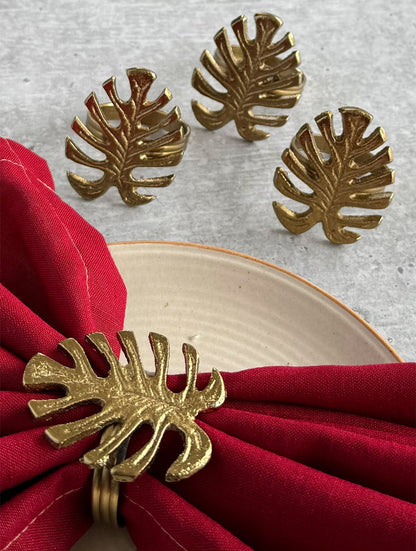 Set of gold monstera leaf napkin rings beside a red napkin and cream plate
