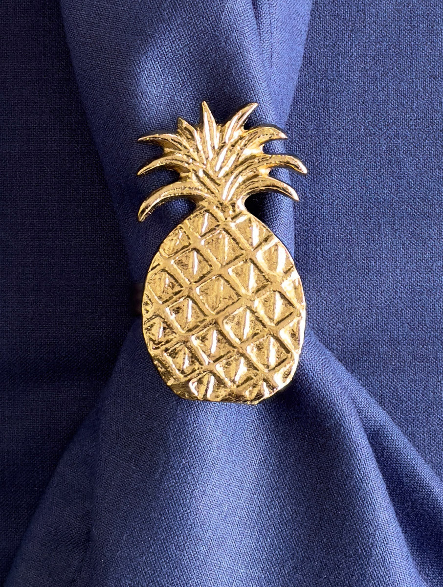 Close-up of a textured gold pineapple napkin ring on a blue linen napkin