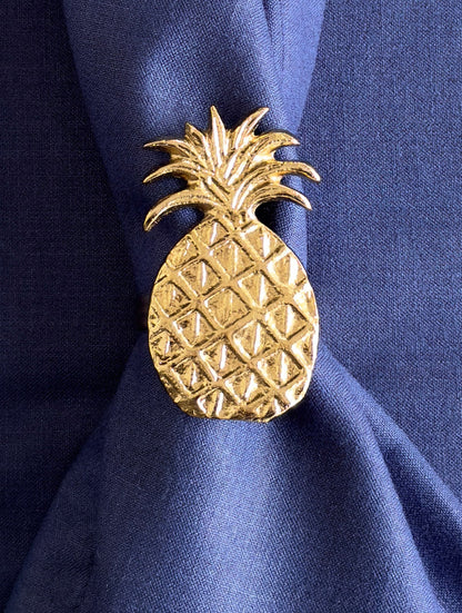 Close-up of a textured gold pineapple napkin ring on a blue linen napkin