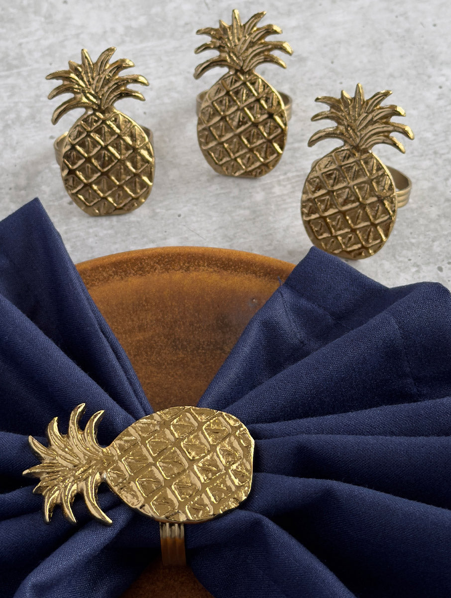 Set of gold pineapple napkin rings with one wrapped around a navy napkin