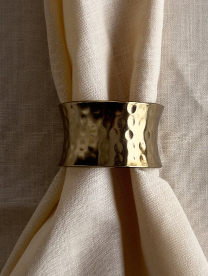 Close-up of a wide hammered gold napkin ring around a cream linen napkin