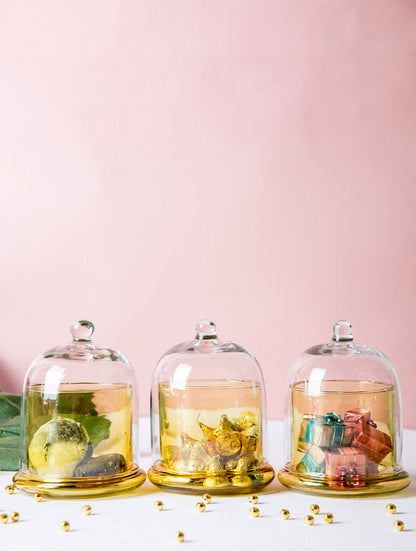 Set of three honey-yellow glass bell jars in a row against a pink wall