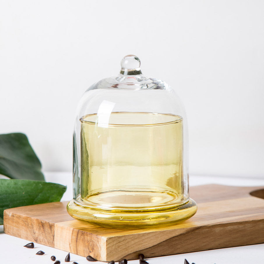 Handmade glass bell jar with a honey-yellow base and clear cloche lid on a wooden board