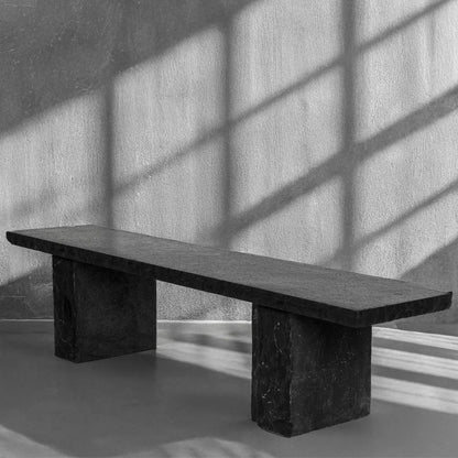 Black marble bench against a textured wall with shadows.