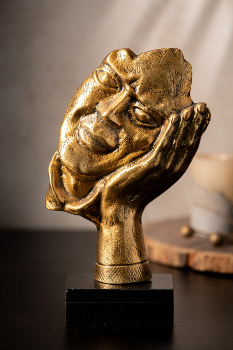 Face resting in a hand sculpture in antique gold