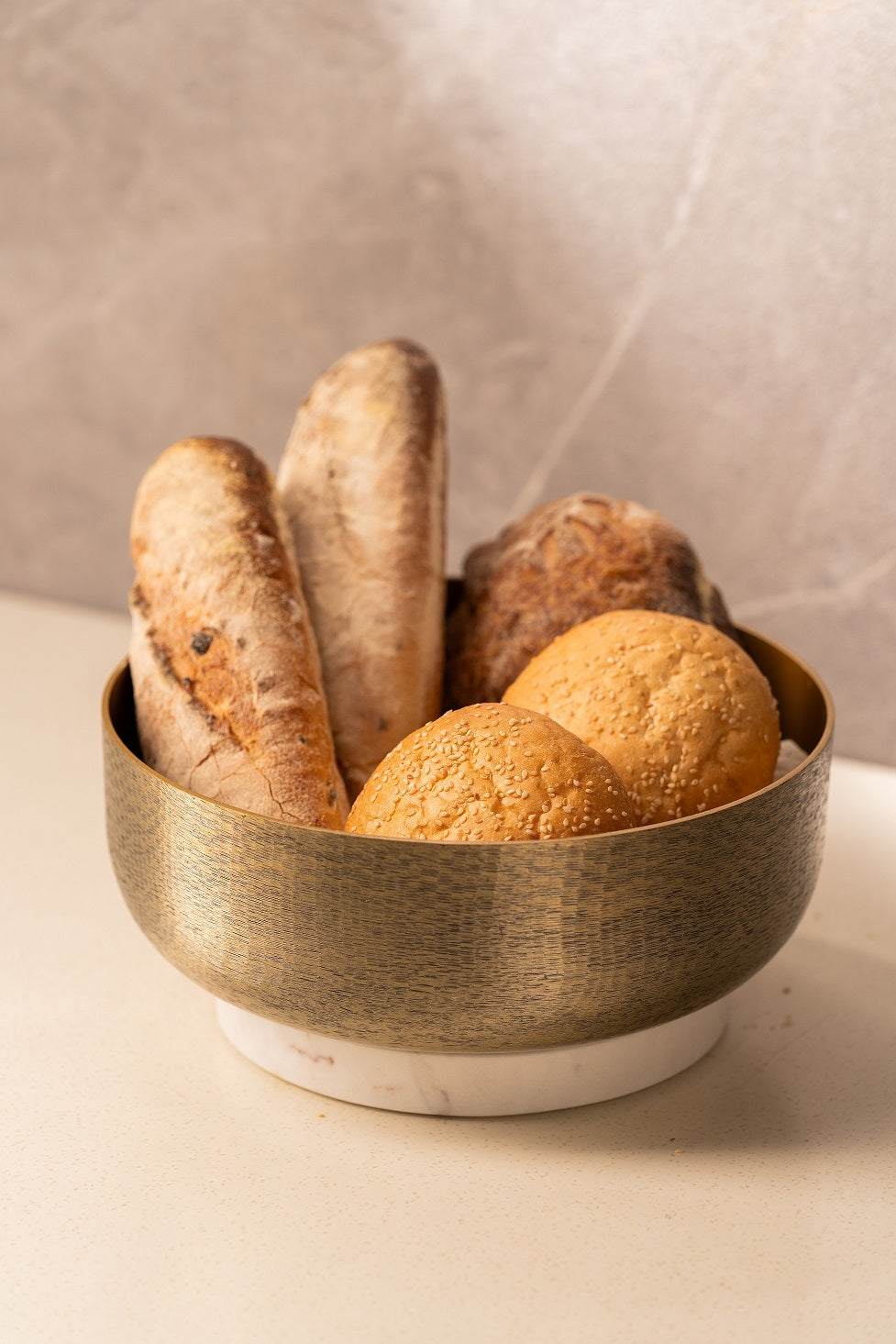 Gold bowl on white marble base styled with baguettes and rolls